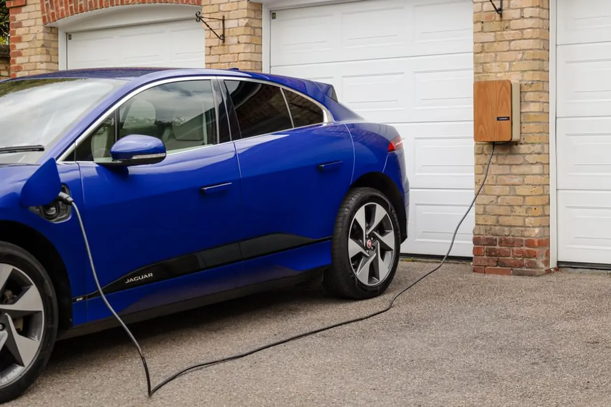 Elektromobil nabíjející se z nástěnné stanice u garáže rodinného domu